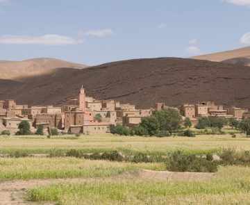 Paysage marocain avec un village à l'arrière-plan ainsi que des reliefs montagneux et de la végétation au premier plan