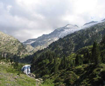 Paysage randonnée à l'Aneto accompagnée par un guide, où l'on peut observer une cascade dans le premier plan et plus haut des montagnes couvertes de neige.