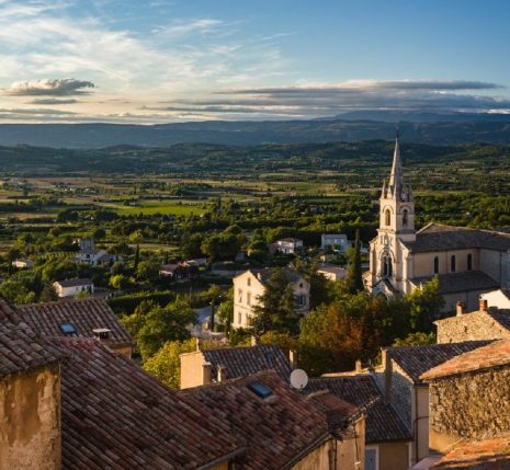 Un village perché dans le Lubéron au premier plan avec en fond une belle vu sur sur paysage avec des montagnes au loin