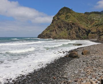 Plage de Madère avec des cailloux noirs sur la plage et un sommet en face, on voit aussi l'océan.