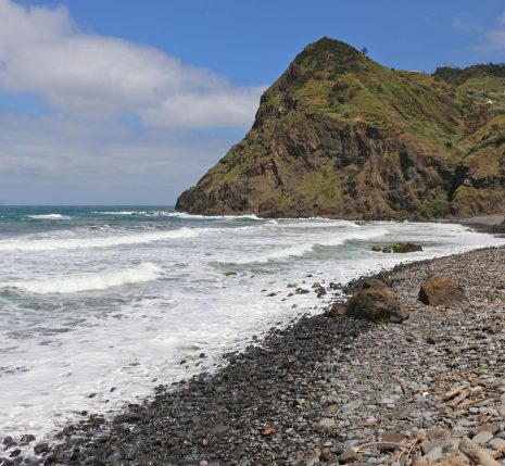 Plage de Madère avec des cailloux noirs sur la plage et un sommet en face, on voit aussi l'océan.