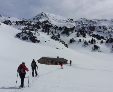 Groupe de marcheurs se dirigeant vers une cabane en pierre dans une étendue de neige avec un fond montagneux.