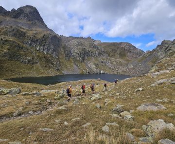 groupe de randonneurs s'avançant sur un sentier avec leur guide dans le massif des Posets, avec un lac en contrebas et des sommets