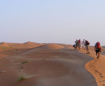 voyage-rando-oman Un groupe de randonneurs dans le désert qui marchent au couché de soleil