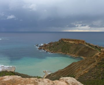 voyage-randonnee-malte-gozo Paysage de bord de mer avec de l'eau turquoise en bord de plage et un sentier montagnard sur les hauteurs